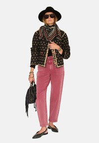 Veste noire brodée avec bordure dorée, foulard noir, pantalon en denim rose, chapeau noir, sac à main noir et ballerines noires cloutées.