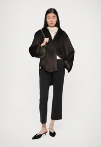 Čierny žebrovaný oversized top so širokými rukávmi, vrstvený na krémovom roláku. Skombinovaný s čiernymi priliehavými nohavicami a čiernymi lodičkami na podpätku. Olivová kabelka.