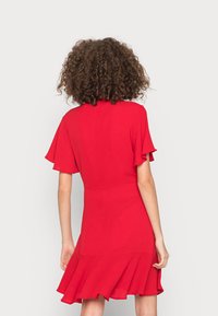 Vestido corto rojo con mangas acampanadas, corsé ajustado y un dobladillo ondulante. Confeccionado en una tela ligera de textura suave.