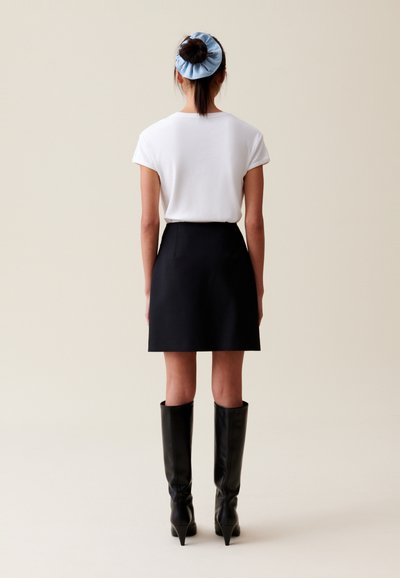 Minifalda negra combinada con una camiseta blanca, complementada con botas negras hasta la rodilla y un coletero azul claro.