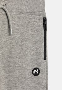 Gray joggers made of soft fabric feature a black zippered pocket, a drawstring waistband, and a circular black logo on the side.