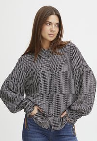 Camicia a maniche lunghe a righe bianche e nere con una vestibilità rilassata, maniche a sbuffo e orlo curvo, abbinata a jeans in denim scuro.