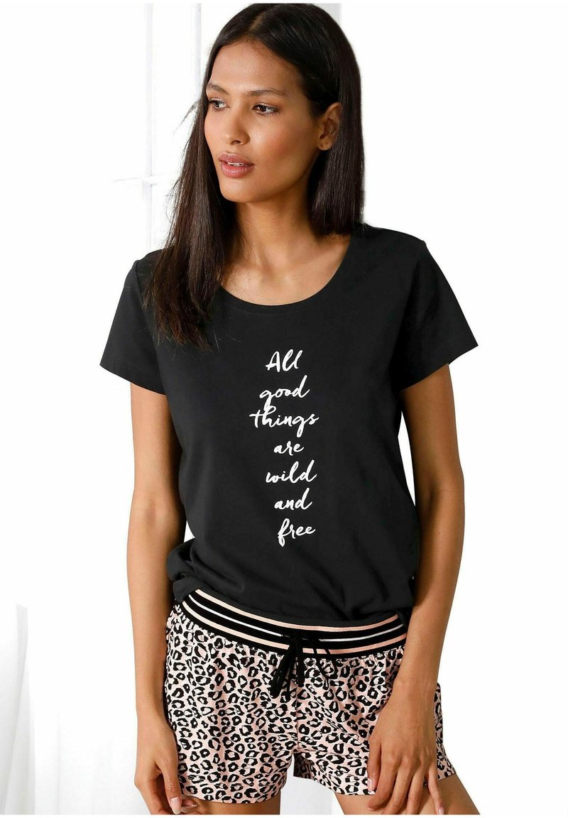 Zwarte t-shirt met korte mouwen met een witte tekstontwerp waarop staat "Alle goede dingen zijn wild en vrij," gecombineerd met roze luipaardprint shorts.