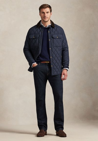 Polstirana mornarsko modra jakna z rjavim kordirnim ovratnikom, z dvema sprednjima žepoma, nošena čez mornarsko modro jopico in temne kavbojke ter rjave čevlje.