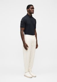 Granatowa koszulka polo z klasycznym kołnierzykiem i krótkimi rękawami, w połączeniu z kremowymi spodniami w wzory oraz białymi tenisówkami. Czysta, nowoczesna estetyka.