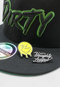 Mustapamppu, jossa on vihreällä brodeerattu "DIRTY", sisältäen kaksi pinniä: keltainen tippuva hymy ja musta "Naughty League" -logo, pyöreä holografinen tarra.