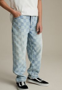 Lichtblauwe geblokte denim jeans met een relaxte pasvorm, voorzien van een rechte pijp en opgerolde zoom, gecombineerd met zwarte sneakers.