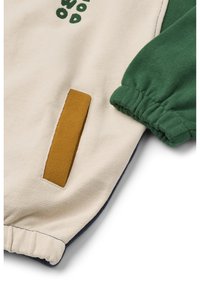 Cotton sweatshirt in cream with green sleeves, featuring a mustard patch pocket and decorative green text. Elasticated cuffs and hem.