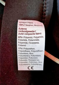 Label met details over textielsamenstelling: 100% neopreen, 83% polyamide, 17% polyurethaan. Duidelijke print, witte achtergrond, zwarte tekst.
