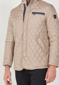 Beige quiltad jacka med blixtlåsförslutning, med en marinblå bröstficka och sidofickor. Slät tyg, strukturerad passform och texturerat diamantmönster.