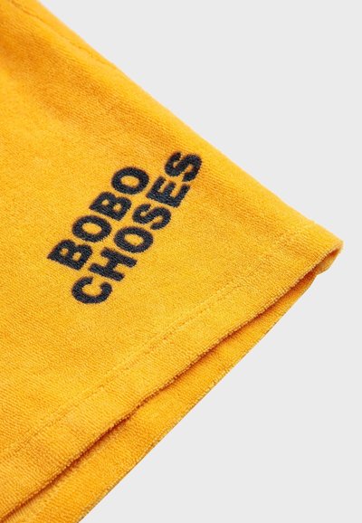 Gul bomullshandduk med en texturerad yta och broderad svart text "BOBO CHOSES" på en kant.