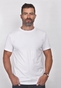 Weißes Baumwoll-T-Shirt mit rundem Hals, kurzen Ärmeln und glatter Textur. Kombiniert mit dunklen Jeans und einem Armband am Handgelenk.