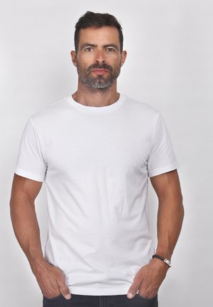 T-shirt en coton blanc avec un col rond, des manches courtes et une texture lisse. Porté avec un jean foncé et un bracelet au poignet.
