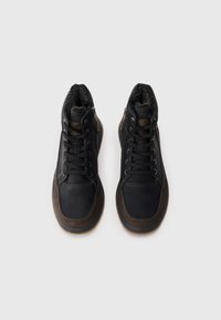 Zapatos altos en negro y marrón con un exterior sintético texturizado, cordones en la parte delantera, cremalleras laterales y un cuello suave forrado de pelo.