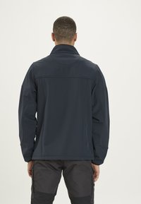 Veste softshell bleu marine avec col montant, manches longues et poignets élastiques. Elle présente une texture lisse et un design minimaliste.