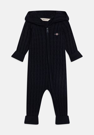 Bodysuit en maille torsadée marine avec une capuche, des manches longues et des poignets côtelés. Comprend une fermeture éclair à l'avant et un petit logo brodé sur la poitrine.
