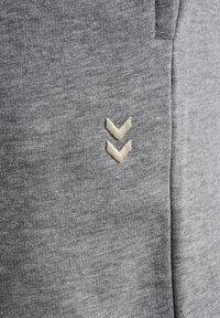 Un tissu gris clair avec une finition texturée présente un logo brodé. Le design comprend deux formes en chevron en blanc cassé.