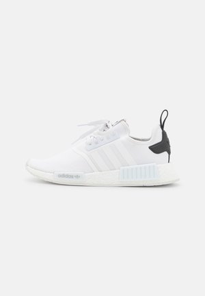 Biały sneaker Adidas NMD z siateczkową cholewką, trzema paskami, białymi sznurówkami i czarną pętlą na pięcie na białym tle.