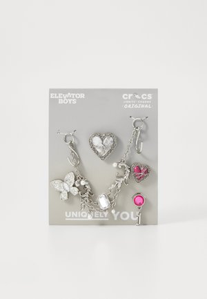 Set di charm in argento con bracciale, caratterizzato da design a farfalla, cuore e gemme, con collegamenti a catena, su una scheda grigia etichettata "Unicamente Te".