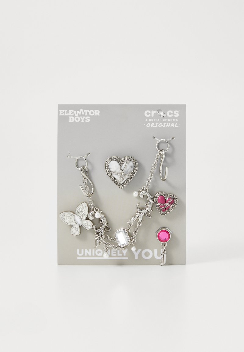 Ensemble de charms en argent comprenant des motifs de papillon, de cœur et de gemmes, avec des maillons de chaîne, présenté sur une carte grise portant l'inscription "Uniquement Vous."