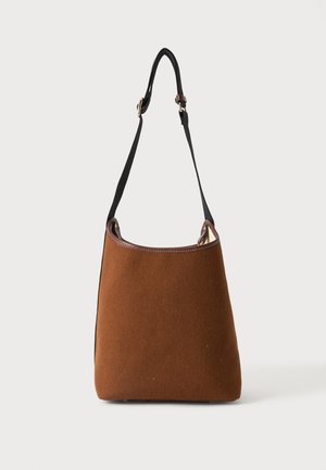 Sac seau en daim marron avec bandoulière noire réglable et garniture en cuir marron foncé sur un fond clair uni.