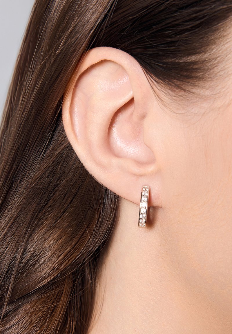 Złoty różowy kolczyk w kształcie koła z osadzonymi przezroczystymi kryształami, prezentujący gładką powierzchnię i okrągły kształt, noszony na małżowinie usznej modelki.