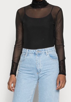 Schwarzes Langarmtop aus transparenter Mesh-Optik mit taillierter Passform. Kombiniert mit hochgeschnittenen hellblauen Jeans im klassischen Schnitt.