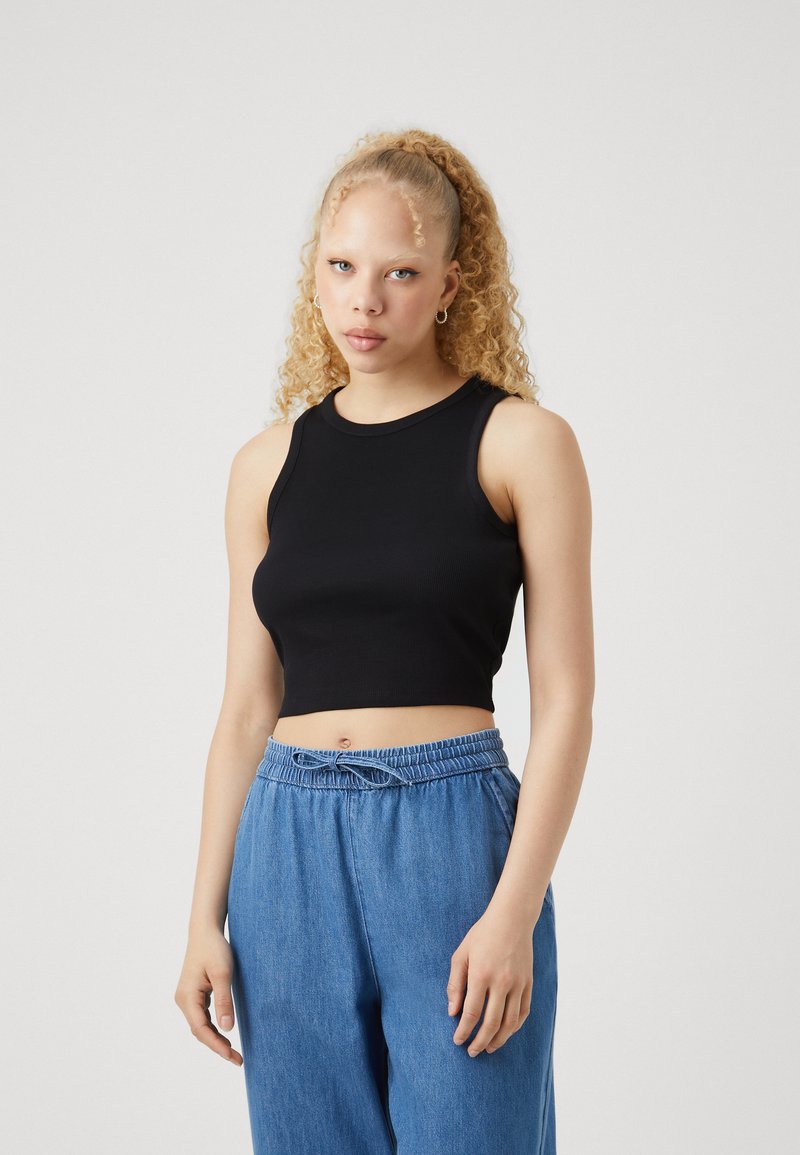 Svart ribbad crop top med rund halsringning, ärmlös design, i kombination med ljusblå byxor med dragsko, som har en avslappnad passform.