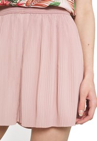 Falda plisada en rosa claro con una cintura texturizada. La tela de la falda es suave, fluida y presenta pliegues verticales que crean una silueta delicada.