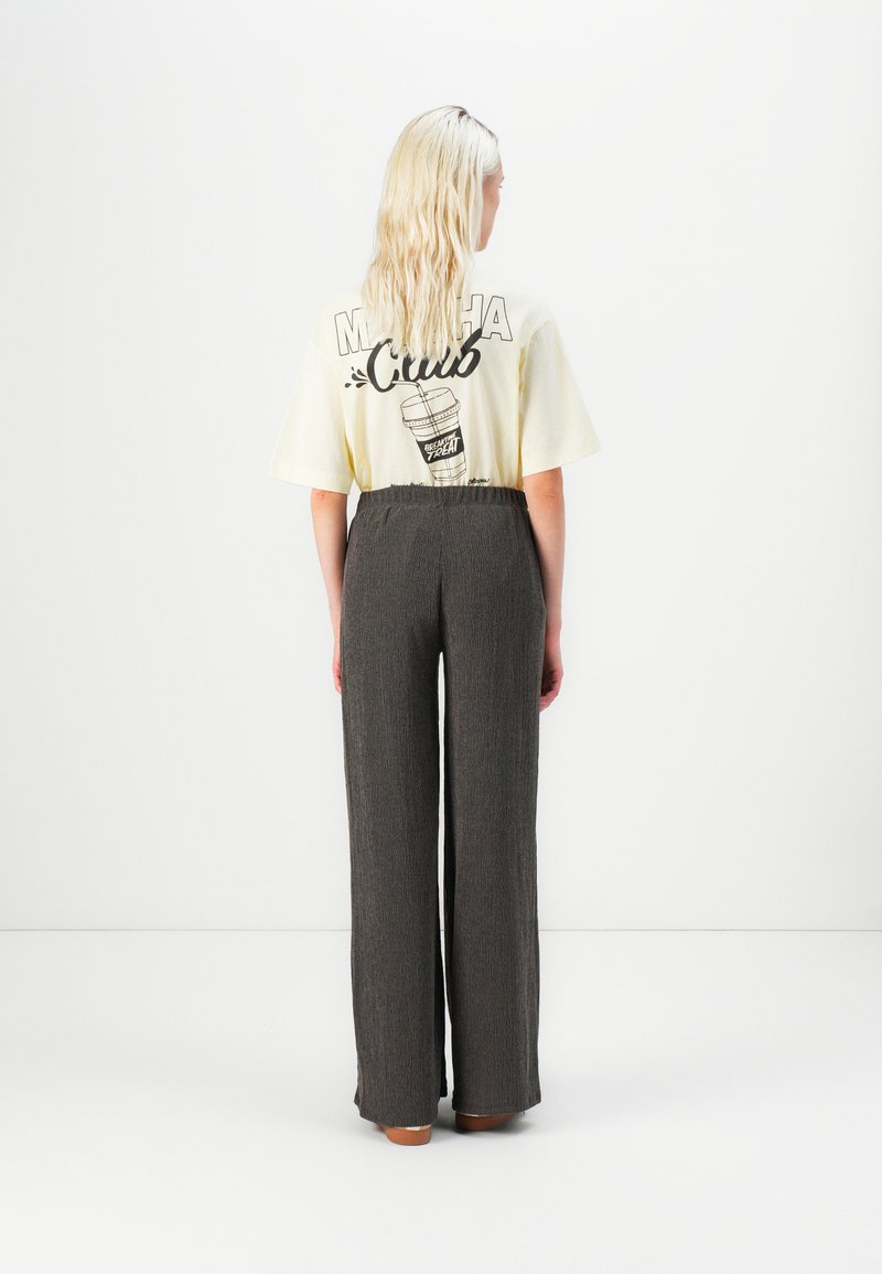 Geel graphic t-shirt met zwarte opdruk op de achterkant, gecombineerd met grijze wijde broek met een gestructureerde stof.