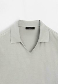 Hellgraues Polohemd mit kurzen Ärmeln, weichem Kragen und V-Ausschnitt, mit einem schwarzen Etikett mit der Aufschrift Massimo Dutti.