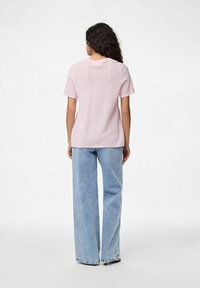 Světle růžový pletený top s krátkým rukávem a texturovaným vzorem, kombinovaný s vysokoklasými světle modrými širokými džíny. Detaily s vroubkovaným lemem.