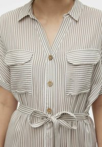 Abito camicia in tessuto leggero, con righe verticali beige e bianche, due tasche sul petto e una cintura in vita annodata.