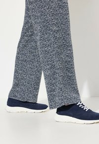 Navy textuur wijde broek gecombineerd met navy suède sneakers met een witte rubberen zool en witte veters.