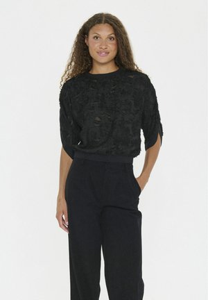 Black textured top with short sleeves and a round neckline, paired with high-waisted dark trousers. The fabric features a patterned finish.