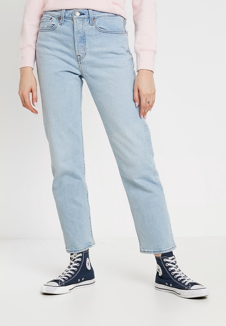 Jeans en denim bleu clair avec une coupe droite, taille haute et style classique à cinq poches, associés à des baskets montantes bleu marine.
