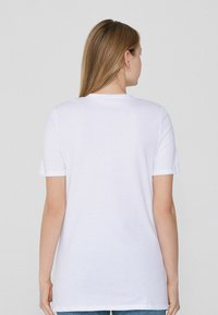 Camiseta de algodón blanca con cuello redondo y mangas cortas, con un corte recto y una textura suave. La vista trasera muestra simplicidad.