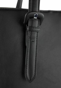 Dettaglio di una borsa a mano in pelle nera con una texture liscia, attacco della tracolla in stile cintura e cuciture eleganti lungo i bordi.