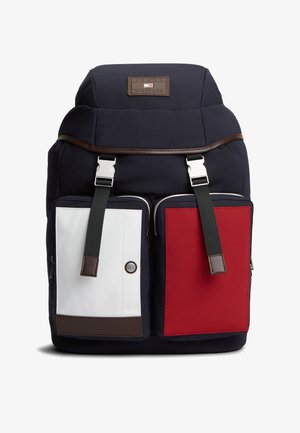 Tamsiai mėlyna kuprinė su rudos spalvos akcentais, turi du priekinės kišenes: vieną baltą, kitą raudoną. Dizainą papildo sidabrinė metalinė detalė ir reguliuojamos juodos petnešos.