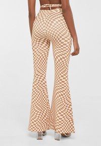 Brązowe i białe spodnie w kratę z szerokimi nogawkami o gładkiej fakturze, wysoki stan oraz dopasowane w biodrach i udach.