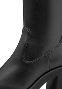 Bottine en cuir noire avec un design élégant, bout rond, panneau latéral élastique et un large talon bloc pour la stabilité.