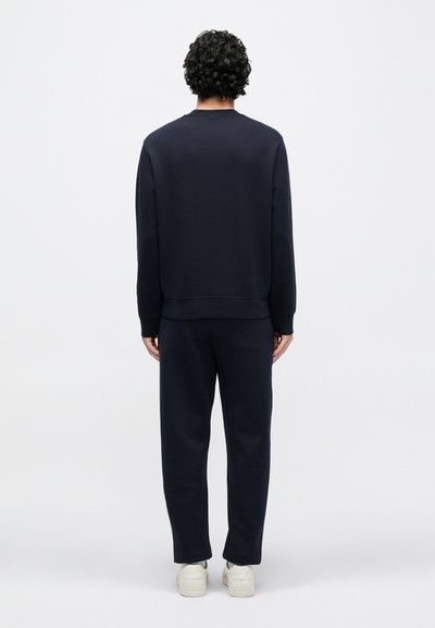 Tmavomodrá mikina a nohavice z mäkkej tkaniny. Neformálny strih s rebrovanými manžetami a pásom, doplnené bielymi teniskami.