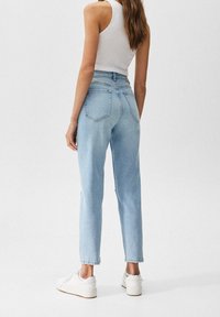 Vaqueros de tiro alto en azul claro con un corte recto, cinco bolsillos y un acabado limpio. Combinados con zapatillas blancas y una camiseta sin mangas ajustada en blanco.