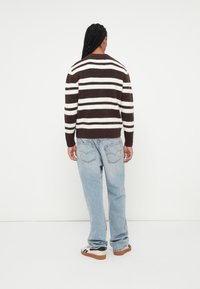 Pull en maille à rayures marron et blanches avec un col rond, des poignets côtelés, associé à un jean en denim bleu clair et des baskets noir et blanc.