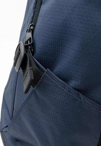 Zaino blu navy caratterizzato da un tessuto testurizzato con motivo a rombi, fissato con accessori neri e dotato di una tasca laterale.