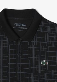 Czarna koszulka polo z graficznym wzorem w ciemnoszarym kolorze. Posiada zapięcie na dwa guziki, kołnierzyk oraz kolorowe logo krokodyla Lacoste. Regularny krój.