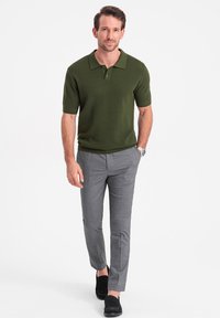 Tmavě zelené polo tričko s krátkým rukávem a texturovaným vzorem, doplněné o světle šedé slim-fit kalhoty a černé nazouvací boty.