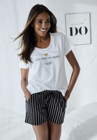Weißes kurzärmliges T-Shirt mit schwarzem Text und einem goldenen Herzdesign. Schwarze Shorts mit weißen vertikalen Streifen und einem elastischen Taillenbund.