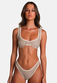 Beige bikini-set met een gestructureerde bralette met brede bandjes en contrasterende afwerking, gecombineerd met hooggeknoopte slips. Zachte textuur.