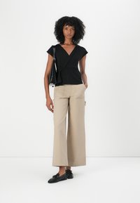 Top negru cu mâneci scurte, tip wrap, cu un detaliu de legare, asortat cu pantaloni largi bej și șlapi negri. Design simplu și curat.